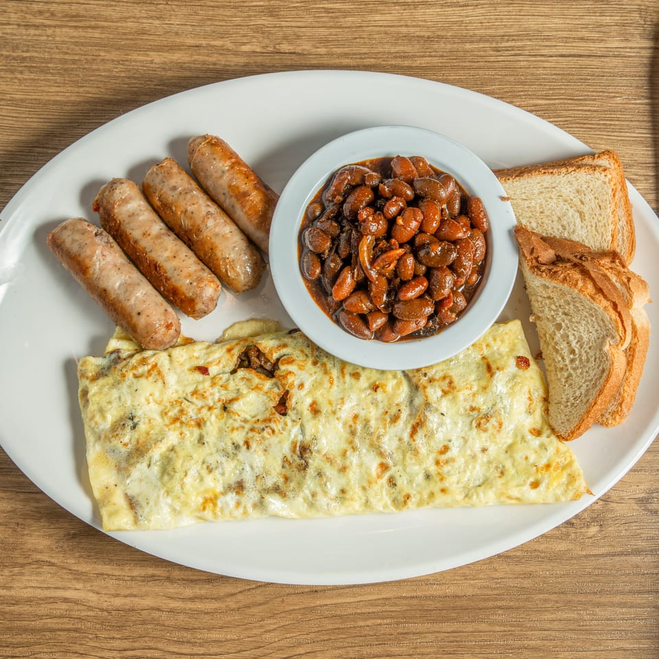 A breakfast platter with sausages, baked beans, an omelet, and toast on a white plate.