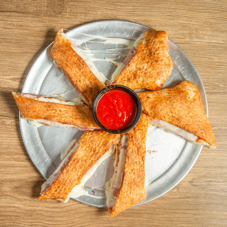 Golden-brown calzone wedges filled with melted cheese and ham, arranged around a cup of marinara sauce.