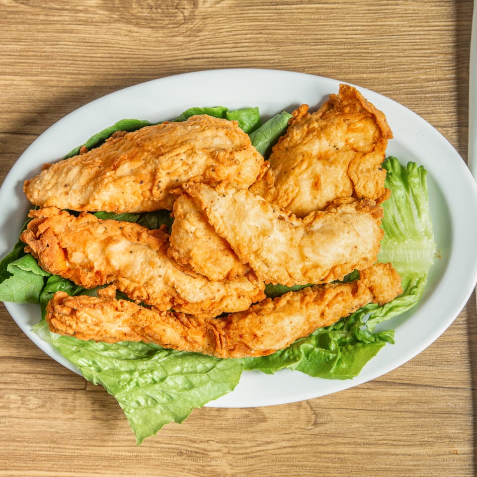 Golden-brown fried chicken tenders on a bed of fresh green lettuce, served on a white plate.