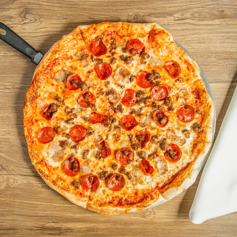 Pepperoni and sausage pizza on a metal peel, next to a white napkin on a wooden table.