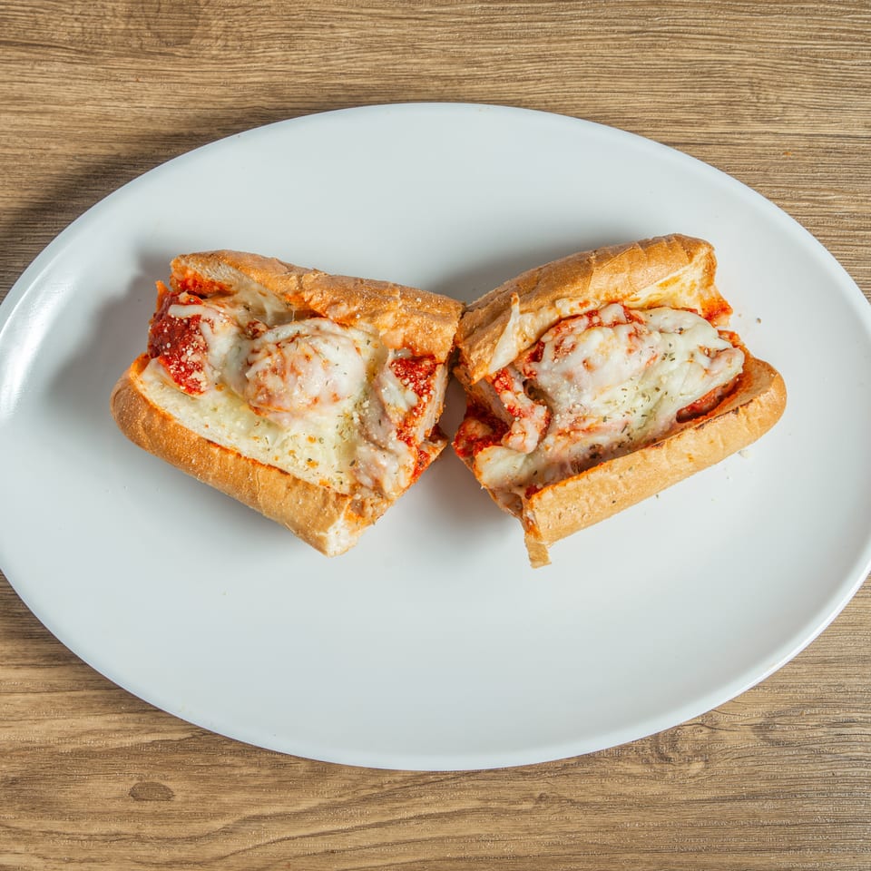 Two halves of a meatball sub sandwich with melted cheese and marinara sauce on a white plate.
